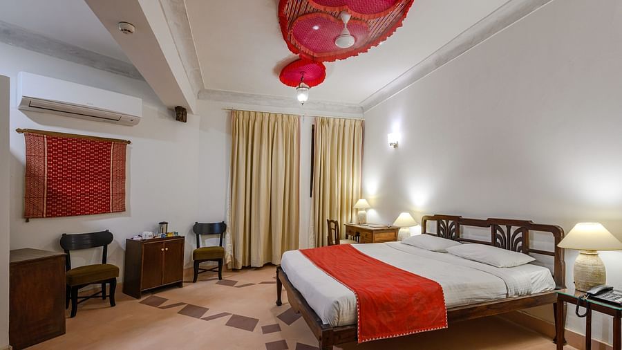 Room with bed, wooden frame, red runner, patterned floor, curtains, furniture including chairs and tables, and decorative ceiling fixtures - Tijara Fort-Palace - 19th Century, Alwar.