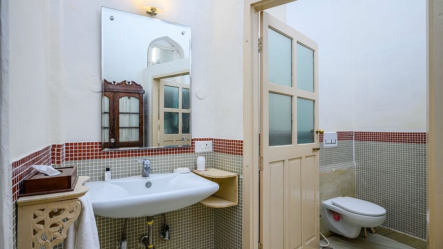 A bathroom with a sink, a mirror, a door with glass panels, and a toilet at Tijara Fort-Palace - 19th Century, Alwar.