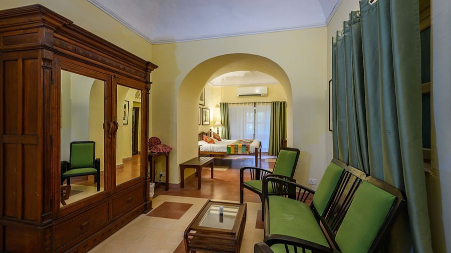 Room with furniture including wardrobe, chairs, and tables, curtains, and view into another room with bed and arched doorway - Tijara Fort-Palace - 19th Century, Alwar.
