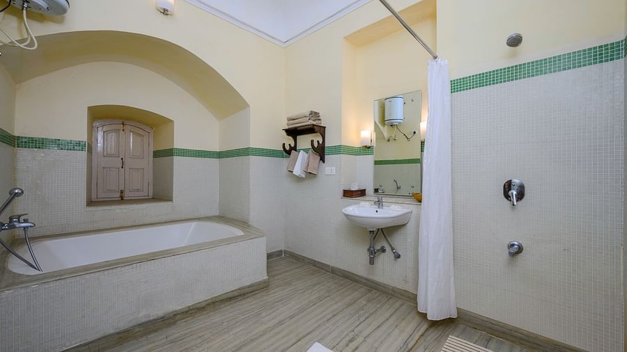 Bathroom with bathtub, sink, mirror, shower curtain, towel rack, arched window, and tiled floor - Tijara Fort-Palace - 19th Century, Alwar.