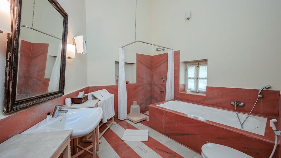 A bathroom with a bathtub, a shower area with a curtain, a sink with a large mirror above it, and a toilet at Tijara Fort-Palace - 19th Century, Alwar.