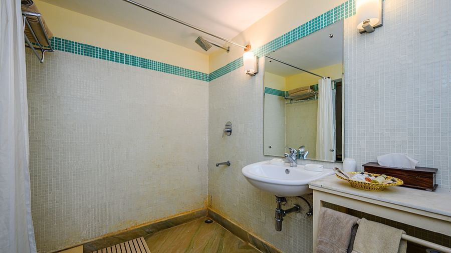Bathroom with a sink, mirror, wall-mounted lights, a shower with a curtain, and a small cabinet with toiletries at Tijara Fort-Palace, Alwar.