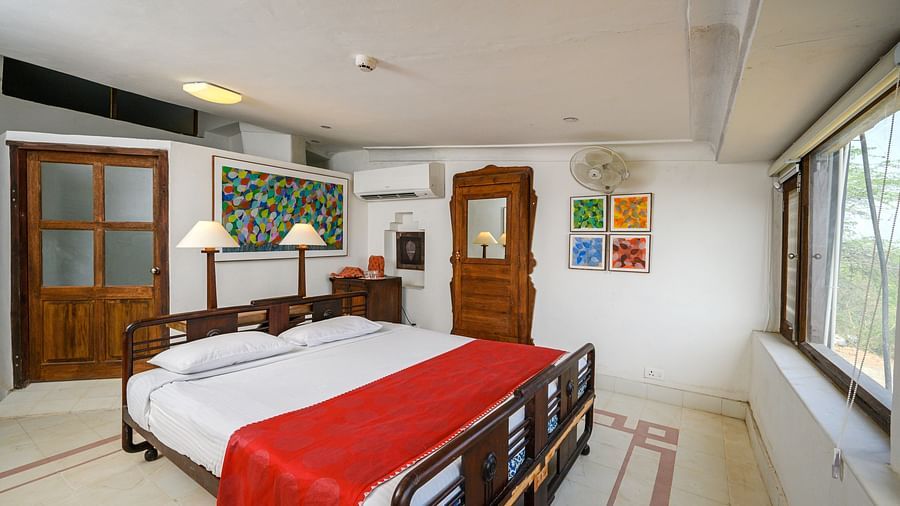 Room with bed, wooden frame, red runner, patterned floor, wooden doors, artwork, mirror, window, and fan - Tijara Fort-Palace - 19th Century, Alwar.