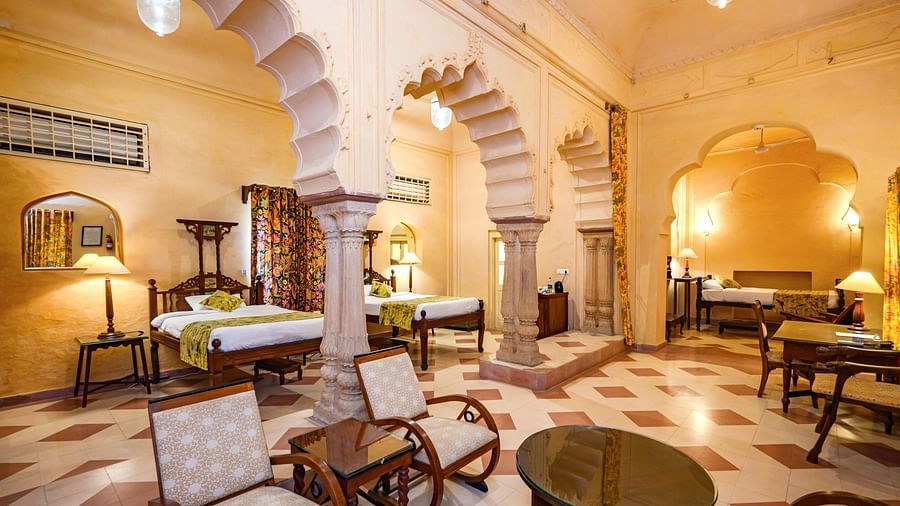 A room with two beds, chairs, tables, lamps, and arched entryways in Tijara Fort-Palace - 19th Century, Alwar.