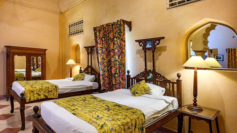 A bedroom with two beds, two side tables with lamps, and a wardrobe in Tijara Fort-Palace - 19th Century, Alwar.