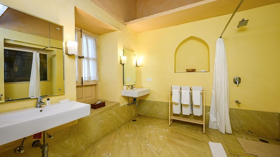 A bathroom with two sinks, mirrors, a shower curtain, and a towel rack with towels in Tijara Fort-Palace - 19th Century, Alwar.
