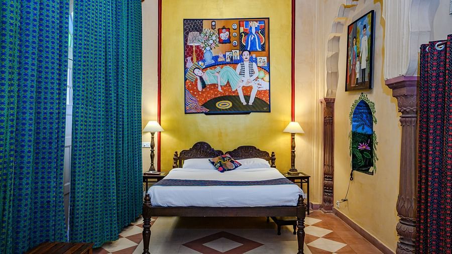 A bedroom with a bed, two side tables with lamps, and two curtains in Tijara Fort-Palace - 19th Century, Alwar.