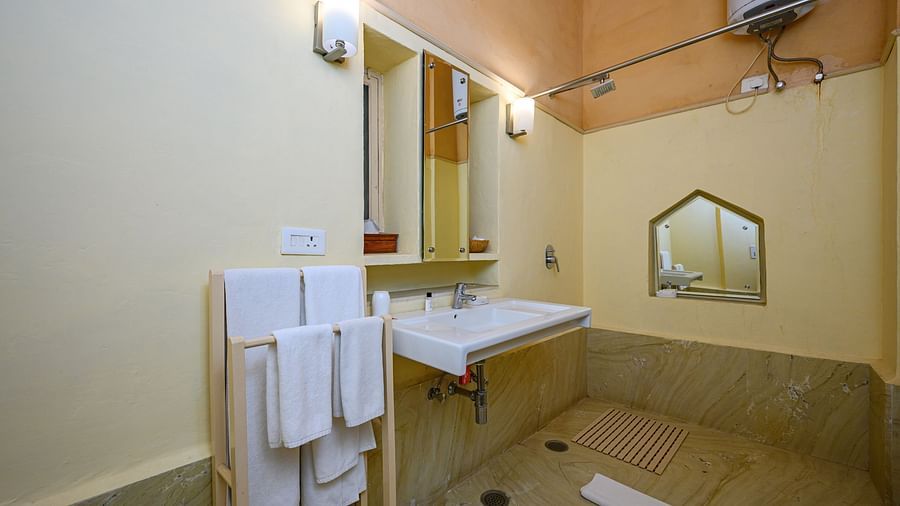 A bathroom with a sink, mirror, towel rack with towels, and a water heater in Tijara Fort-Palace - 19th Century, Alwar.
