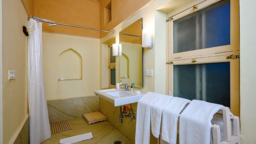 A bathroom with a sink, mirror, shower curtain, and towels in Tijara Fort-Palace - 19th Century, Alwar.