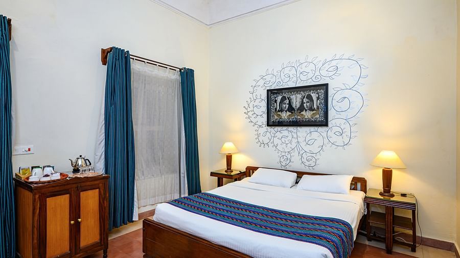A bedroom with a bed, artwork on the wall, curtains, and a cabinet at Tijara Fort-Palace - 19th Century, Alwar.
