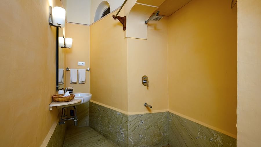 Bathroom with a sink, wall-mounted lights, towels, and a shower area with marble-like tiling at Tijara Fort-Palace, Alwar.