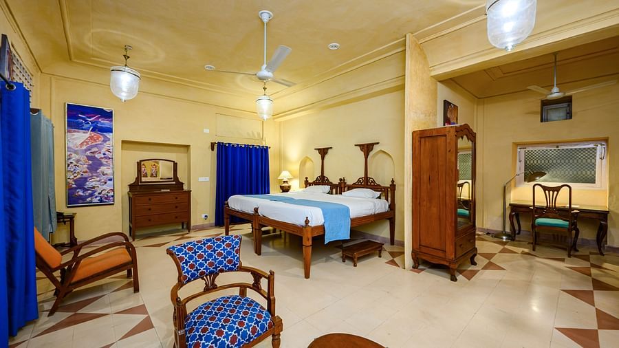 A bedroom with a bed, chairs, a wardrobe, and a desk in Tijara Fort-Palace - 19th Century, Alwar.