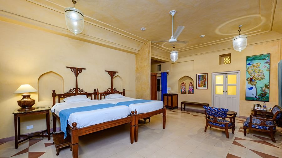 A bedroom with two beds, two side tables, chairs, and a door in Tijara Fort-Palace - 19th Century, Alwar.