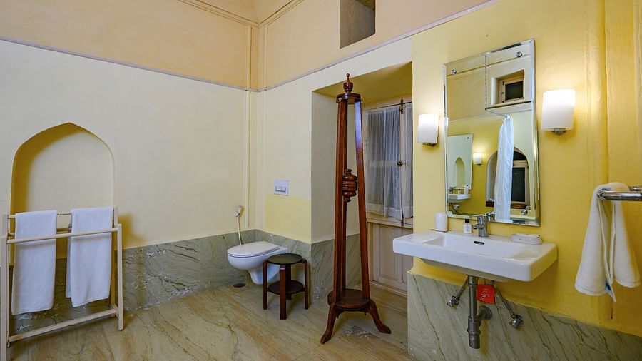 A bathroom with a sink, mirror, toilet, towel rack with towels, and a stand in Tijara Fort-Palace - 19th Century, Alwar.