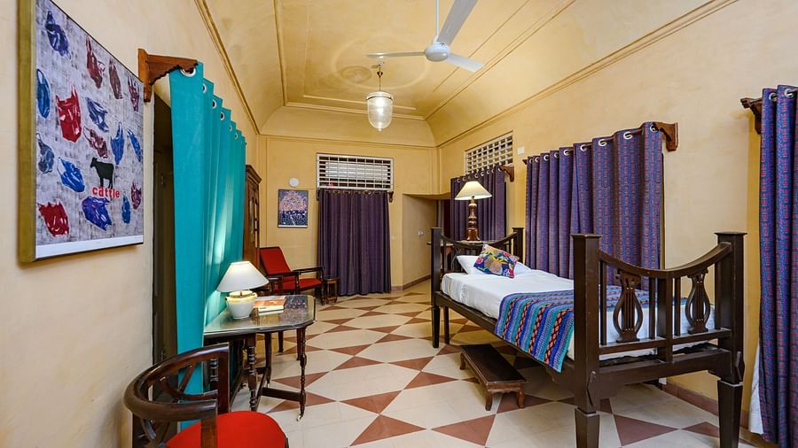 A bedroom with a bed, two chairs, a table, and curtains in Tijara Fort-Palace - 19th Century, Alwar.