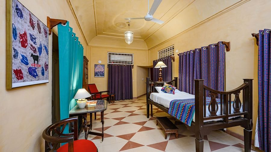 A room with a single bed, a table, seating, and purple curtains dividing the space at Tijara Fort-Palace - 19th Century, Alwar.