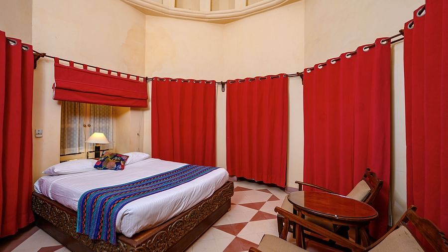 A room with a bed, a table with chairs, and many curtains in Tijara Fort-Palace - 19th Century, Alwar.