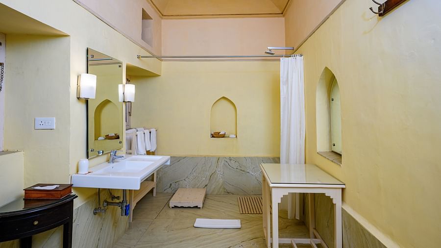 A bathroom with a sink, mirror, shower curtain, and a table in Tijara Fort-Palace - 19th Century, Alwar.