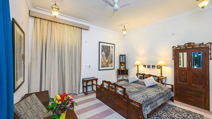 Room with bed, patterned pillows and bedding, furniture including chairs, tables, and a wardrobe, artwork, patterned rug, curtains, decorative ceiling lights, and patterned floor tiles - Neemrana Tijara Fort-Palace.
