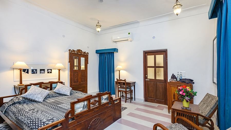 Room with bed, patterned pillows and bedding, furniture including chairs, tables, desk, and wardrobe, curtains, decorative ceiling lights, and patterned floor tiles - Tijara Fort-Palace - 19th Century, Alwar.