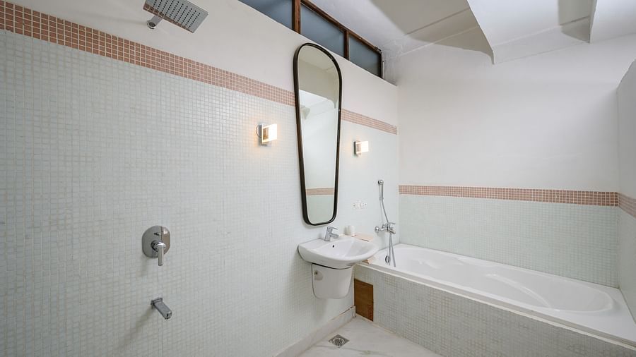 A bathroom with a bathtub, a pedestal sink with a tall mirror above it, and a shower fixture on the wall at Tijara Fort-Palace - 19th Century, Alwar.