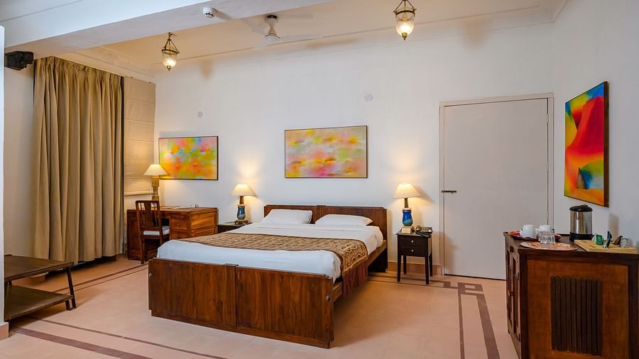 Room with bed, wooden frame, furniture including desks and cabinets, lamps, artwork on walls, curtains, and overhead lighting fixtures - Tijara Fort-Palace - 19th Century, Alwar.