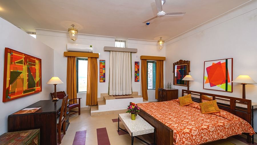 Room with bed, patterned bedding, furniture including desk, chair, tables, and cabinets, artwork, patterned rugs, curtains, decorative ceiling lights, and patterned floor tiles - Tijara Fort-Palace - 19th Century, Alwar.