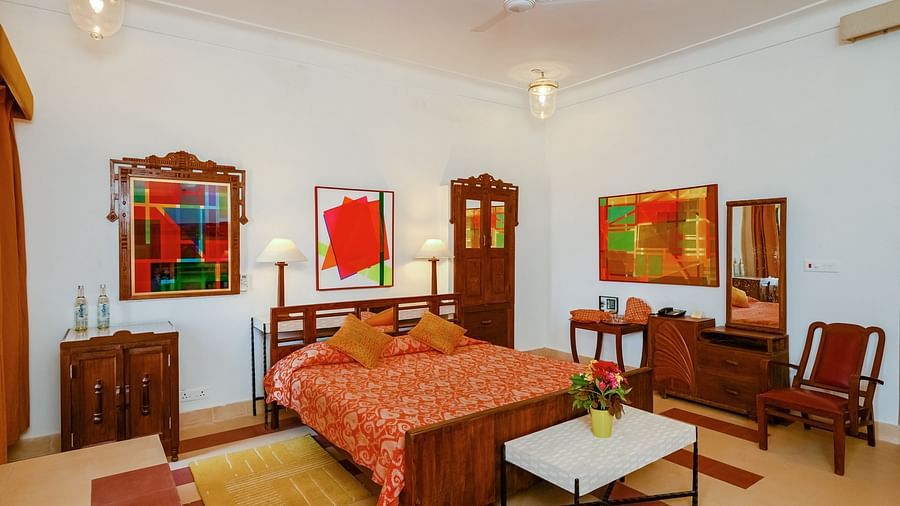 Room with bed, patterned bedding, furniture including tables, chairs, cabinets, and a wardrobe, artwork, patterned rugs, decorative ceiling lights, and patterned floor tiles - Tijara Fort-Palace - 19th Century, Alwar.