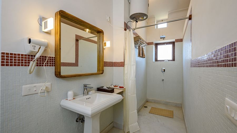 Bathroom with sink, mirror, shower curtain, windows, and wall-mounted hair dryer - Tijara Fort-Palace - 19th Century, Alwar.