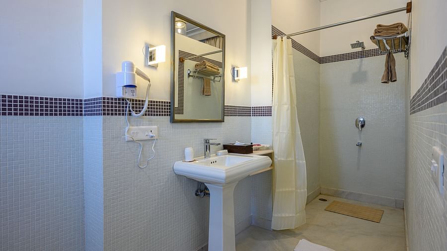 Bathroom with sink, mirror, shower curtain, and wall-mounted hair dryer - Tijara Fort-Palace - 19th Century, Alwar.