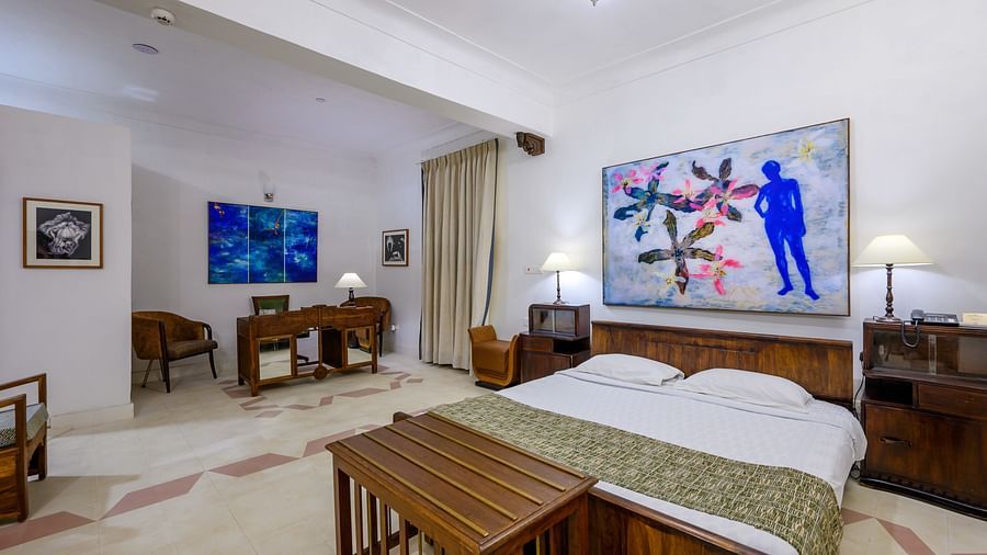 A hotel suite with a bed, wooden furniture including bedside tables and a desk, artwork on the walls, and a seating area at Tijara Fort-Palace - 19th Century, Alwar.
