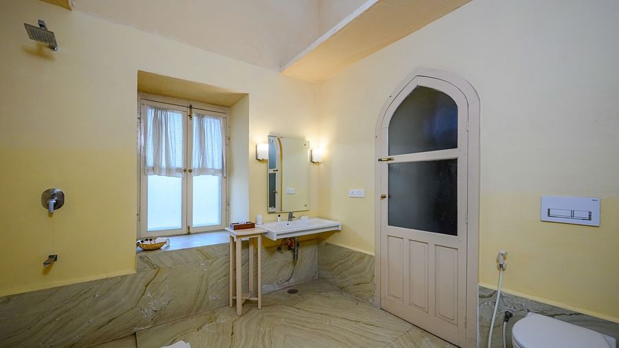 A bathroom with a sink, mirror, toilet, and a door in Tijara Fort-Palace - 19th Century, Alwar.