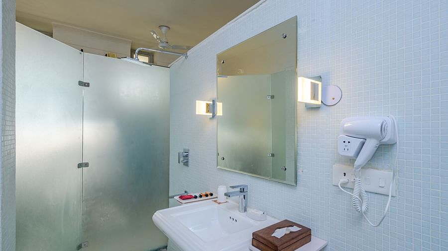 Bathroom with a sink, mirror, toiletries, hairdryer mounted on the wall, and a frosted glass shower enclosure at Tijara Fort-Palace - 19th Century, Alwar.