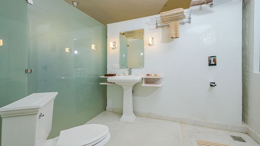 A bathroom with a toilet, a pedestal sink with a mirror above it, and a shower area enclosed with frosted glass at Tijara Fort-Palace - 19th Century, Alwar.
