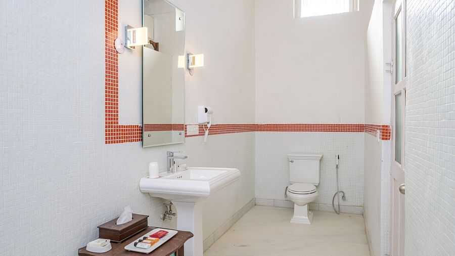 Bathroom with sink, mirror, toilet, small table with items, window, and tiled floor - Tijara Fort-Palace - 19th Century, Alwar.