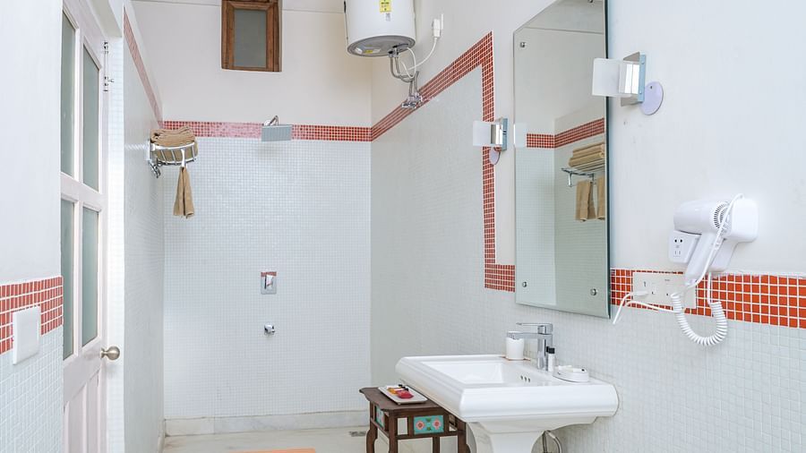 Bathroom with sink, mirror, shower, water heater, wall-mounted hair dryer, small table, window, and tiled floor - Tijara Fort-Palace - 19th Century, Alwar.