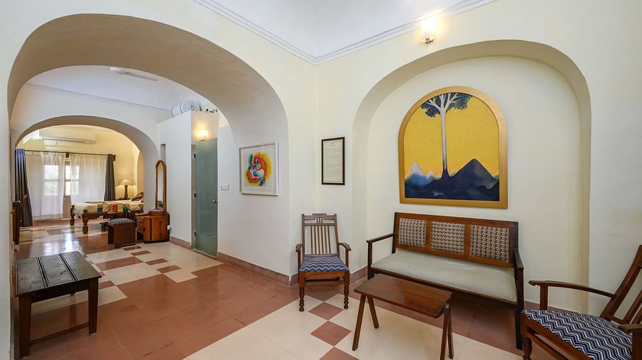 A room with arched openings, benches, chairs, a small table, and artwork on the walls at Tijara Fort-Palace, Alwar.