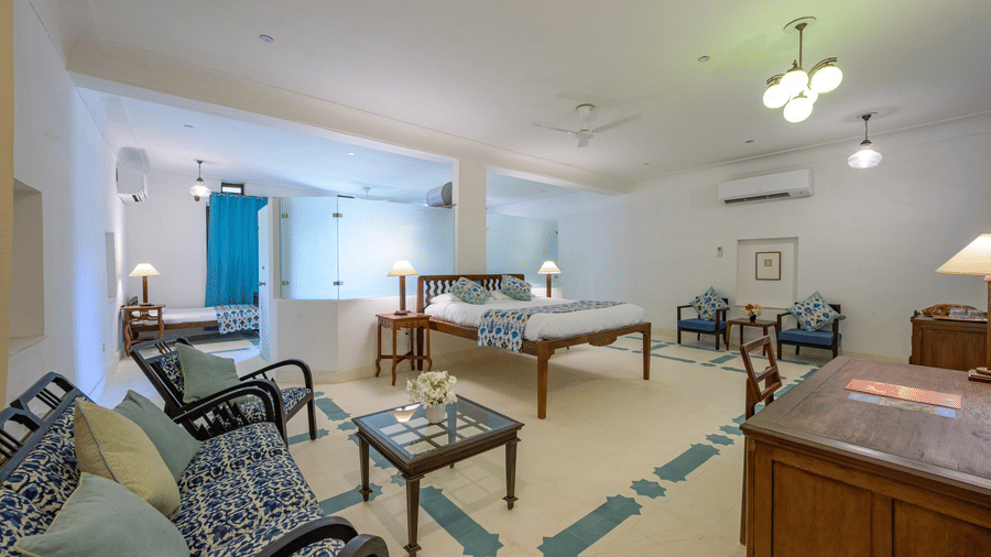 A spacious room with a bed, bedside tables with lamps, multiple seating areas with sofas and chairs around tables, and patterned flooring at Tijara Fort-Palace - 19th Century, Alwar