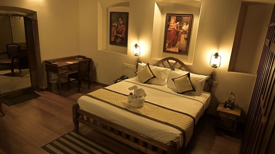 Heritage Suite at Uday Suites under warm lighting featuring a plush bed with bath towels made into an elephant on the bed runner and a work desk near the bed facing the wall while the wall above the headboard features a couple of paintings by Raja Ravi Var
