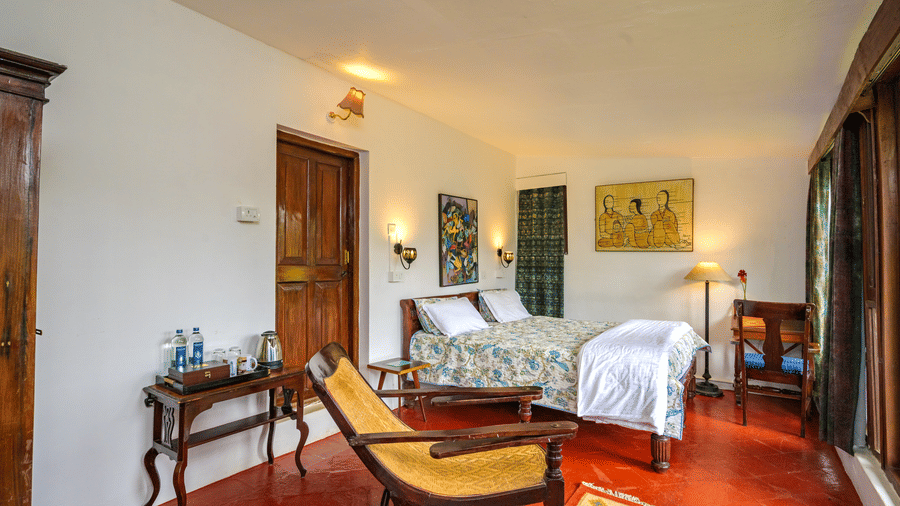 A wide-angle shot of the bedroom of the Eucalyptus - Valley View room featuring a double bed and a reclining arm chair - Wallwood Garden - 19th Century, Coonoor
