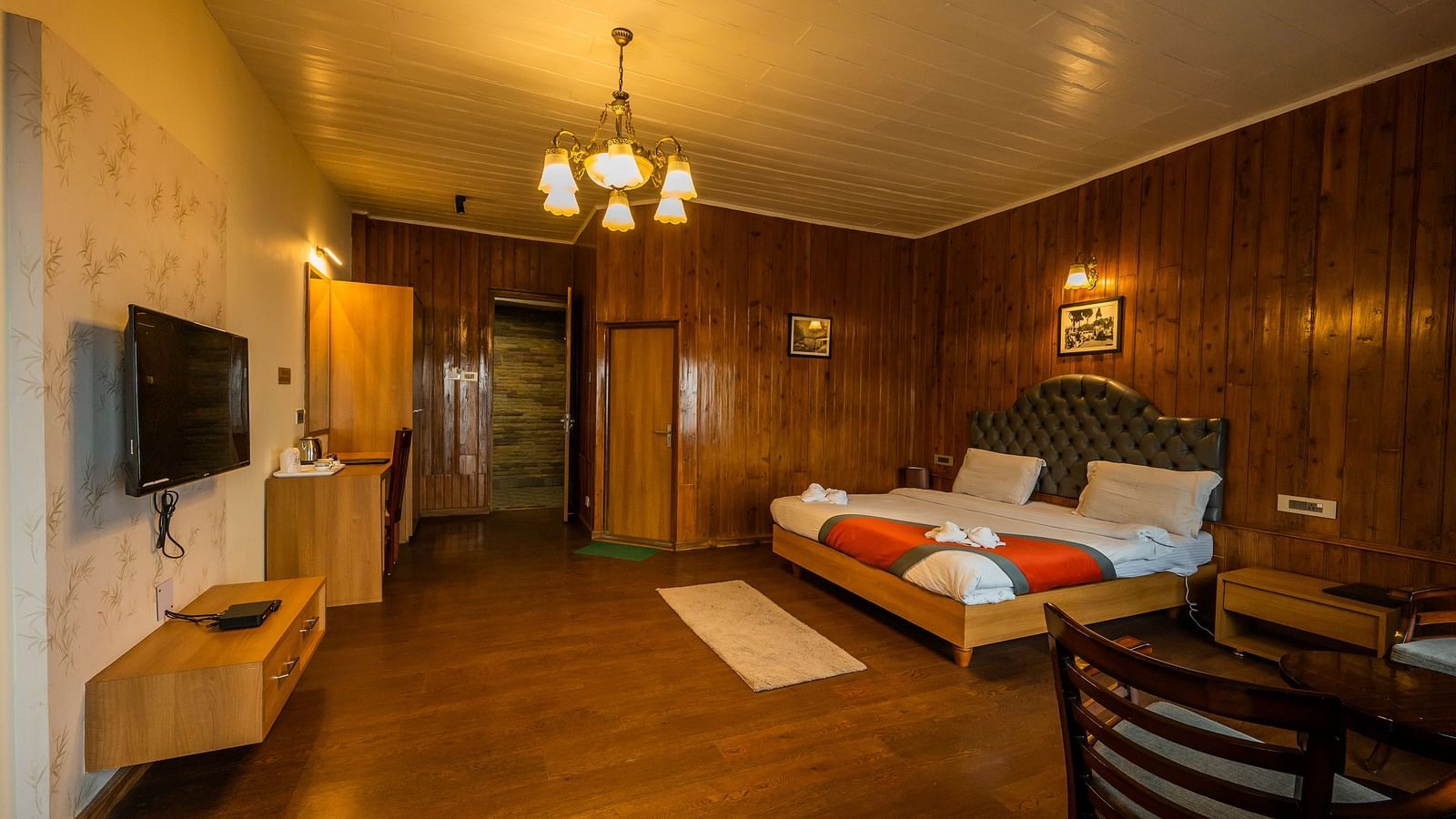 A side angle view of A spacious room with wooden furnished  comfy bed and the have bed side table and chair and Flat screen TV at Arcadia Heritage Resort, Darjeeling