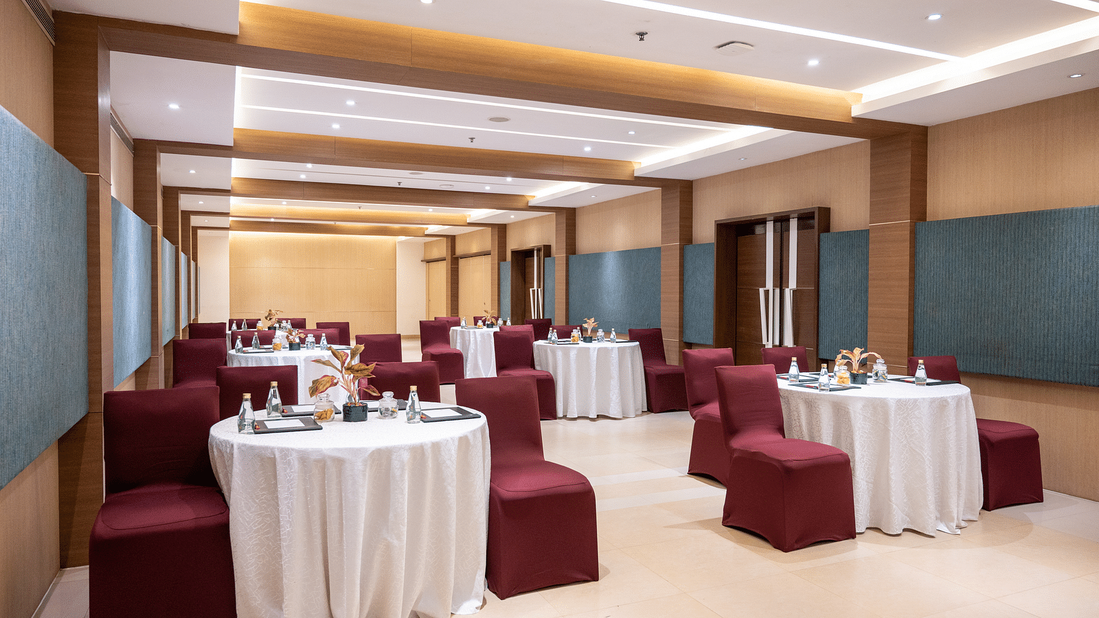 An image of the hall with white round tables and maroon chairs at Grand Kakinada by GRT Hotels