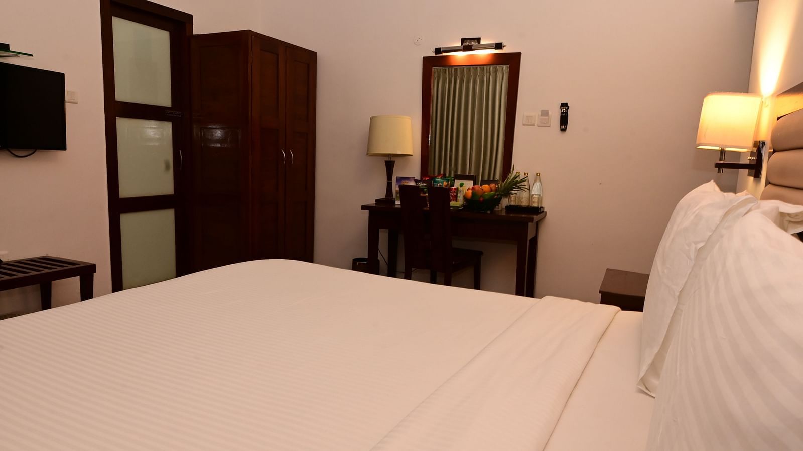 An image of a room with a king size bed, bed side table, lamps, dressing table, and a chair - GReaT trails Kodaikanal by GRT Hotels