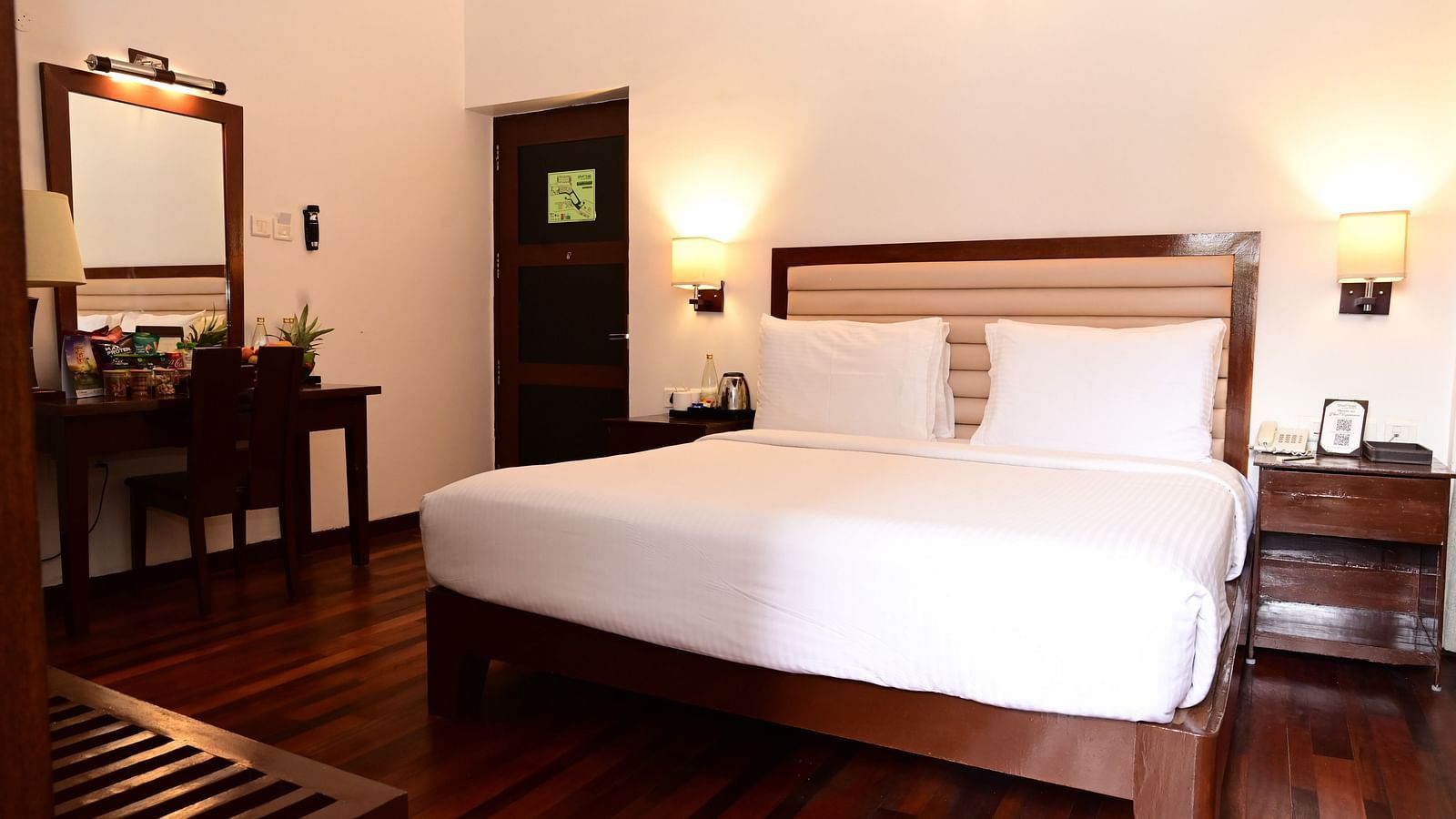 An image of a room with a king size bed, bed side table, lamps, dressing table, and a chair - GReaT trails Kodaikanal by GRT Hotels