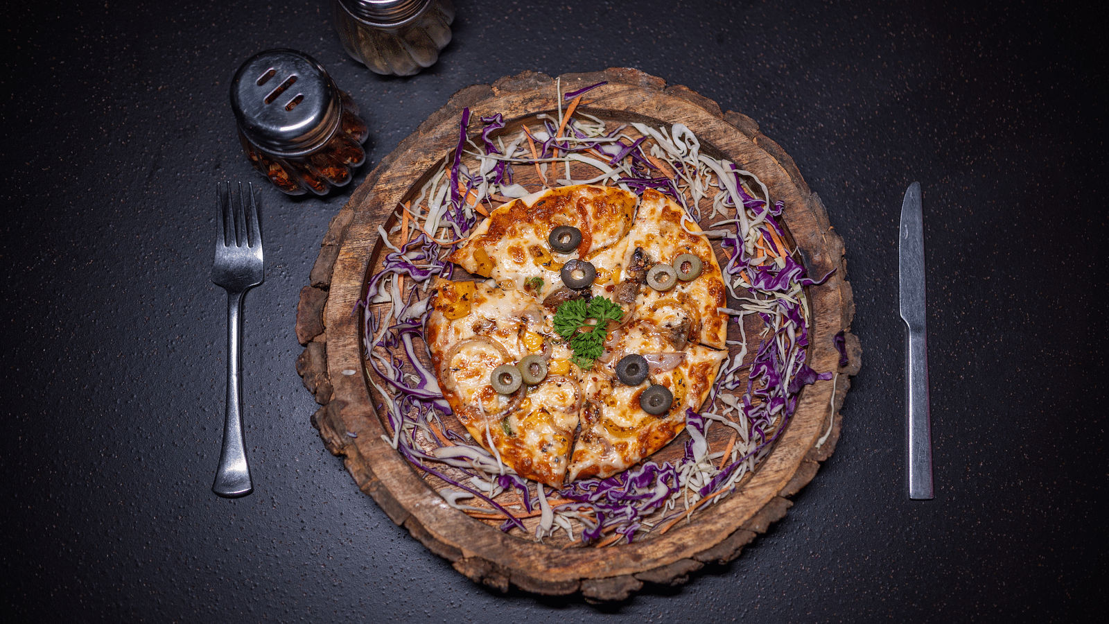 A top view of a pizza topped with a basil leaf, accompanied by cutlery, elegantly arranged at Hotel Moti Palace.