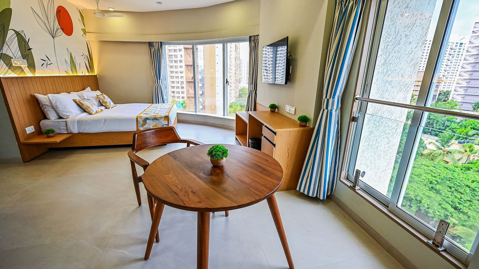 An image of Cozy Double Studio Room featuring a bed, a cabinet, a chair and table set, and a large window at Indie Stays Studio, Chembur