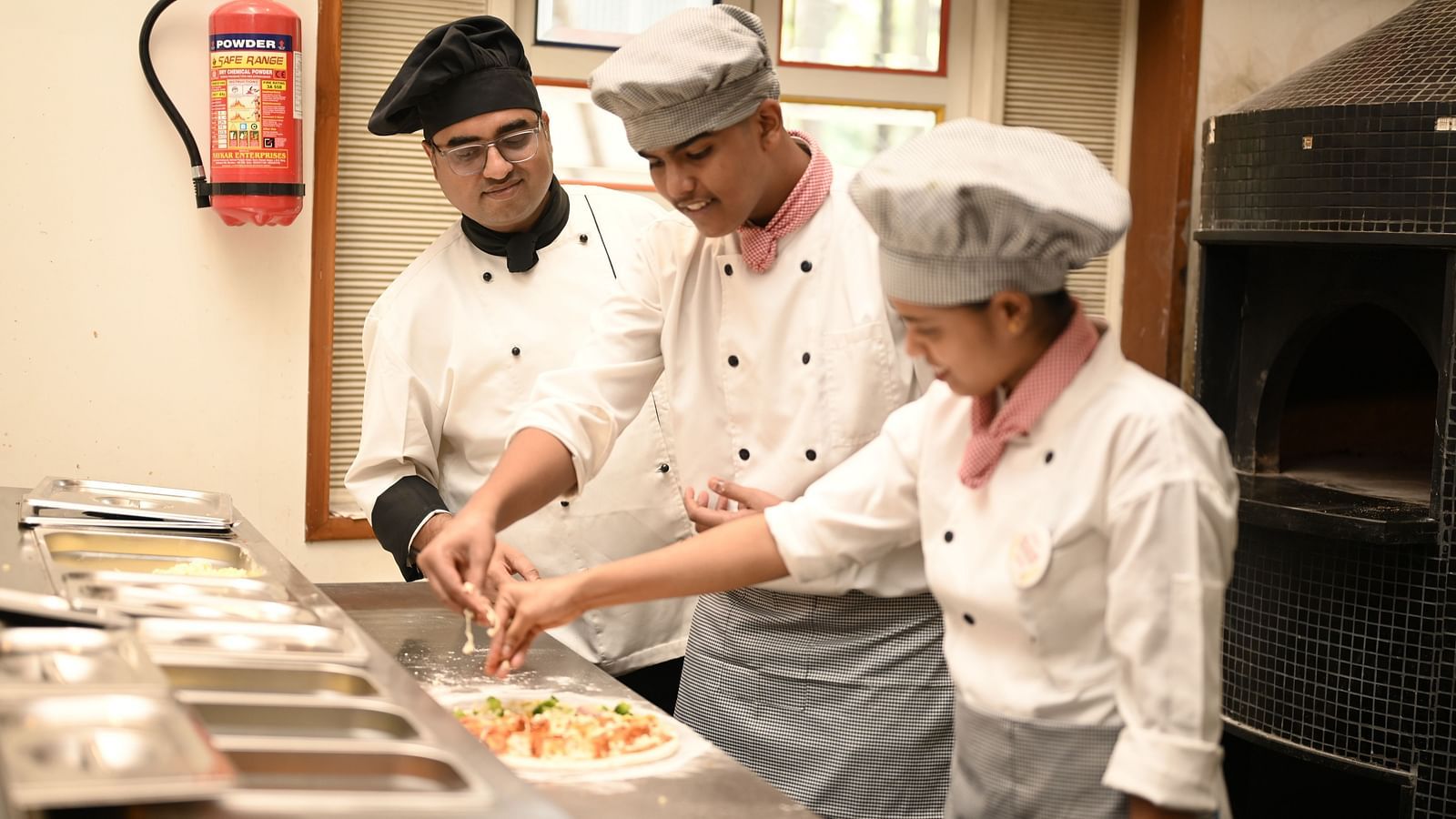 Culinary trainees learning pizza preparation under the guidance of a chef in a professional kitchen - Kamats India