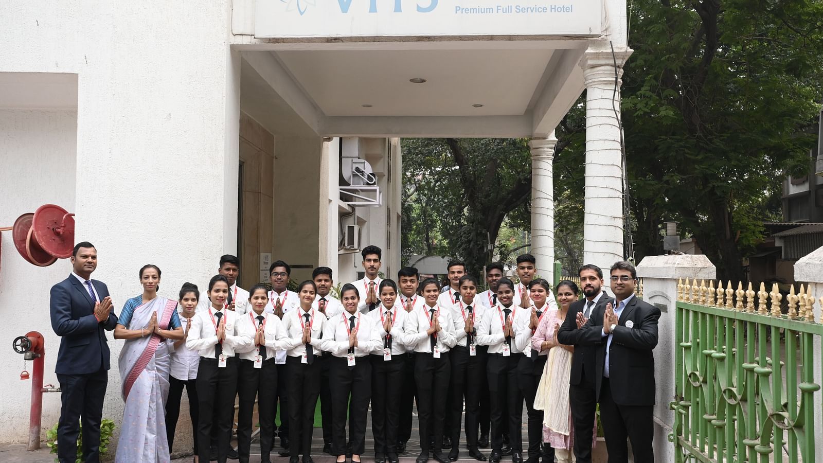Hotel staff and management standing together outside the hotel entrance, greeting with folded hands - Kamats India