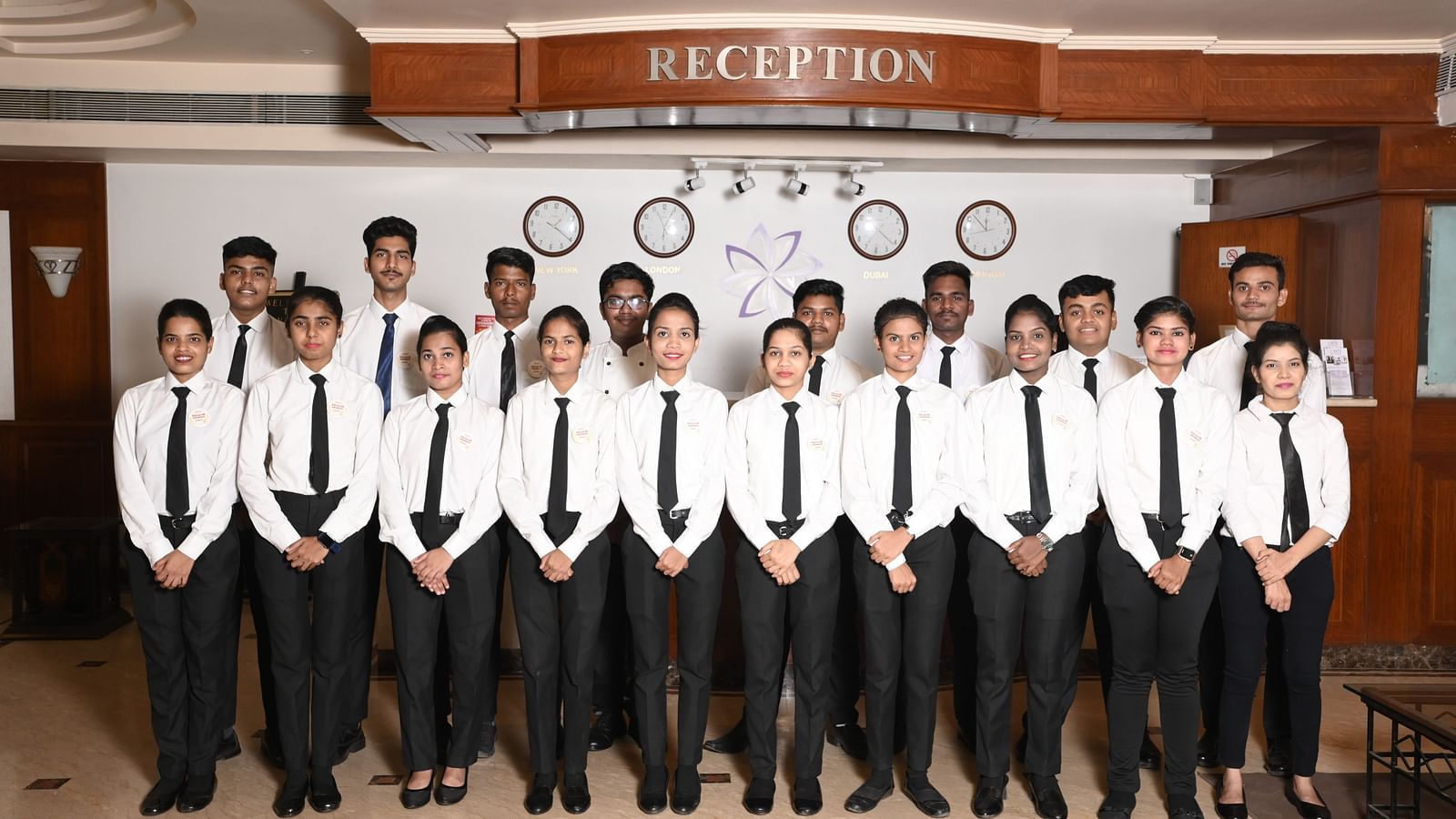 A team of hotel reception staff posing in formal attire in front of the reception desk - Kamats India