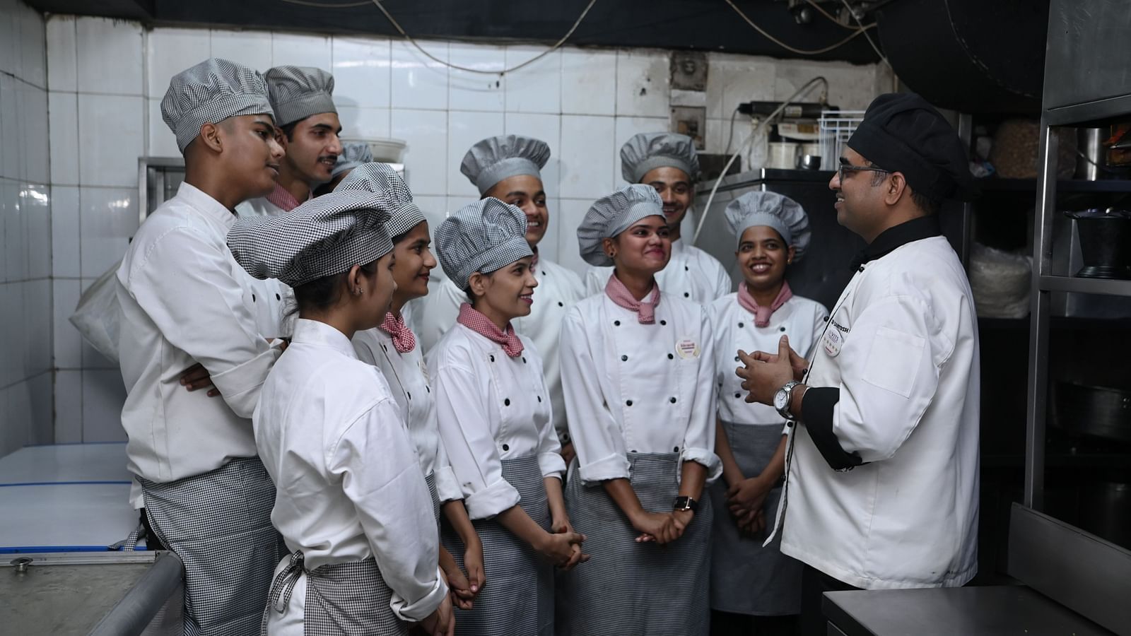 Culinary trainees receiving instructions from a chef in a kitchen environment - Kamats India